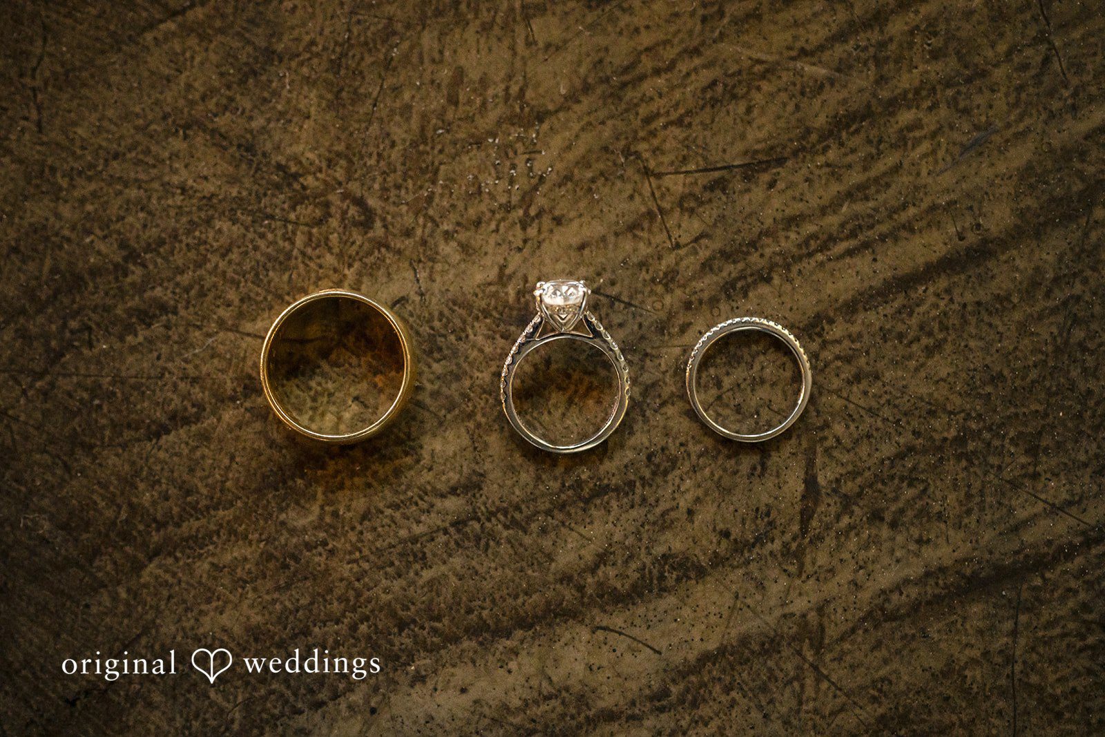 A wedding ring and two wedding bands placed flat on a rustic wooden surface.