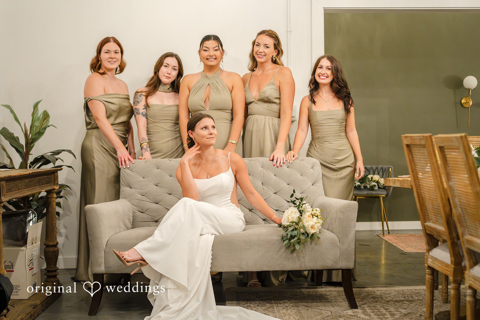 A bride sitting on a sofa surrounded by her bridesmaids in matching dresses.