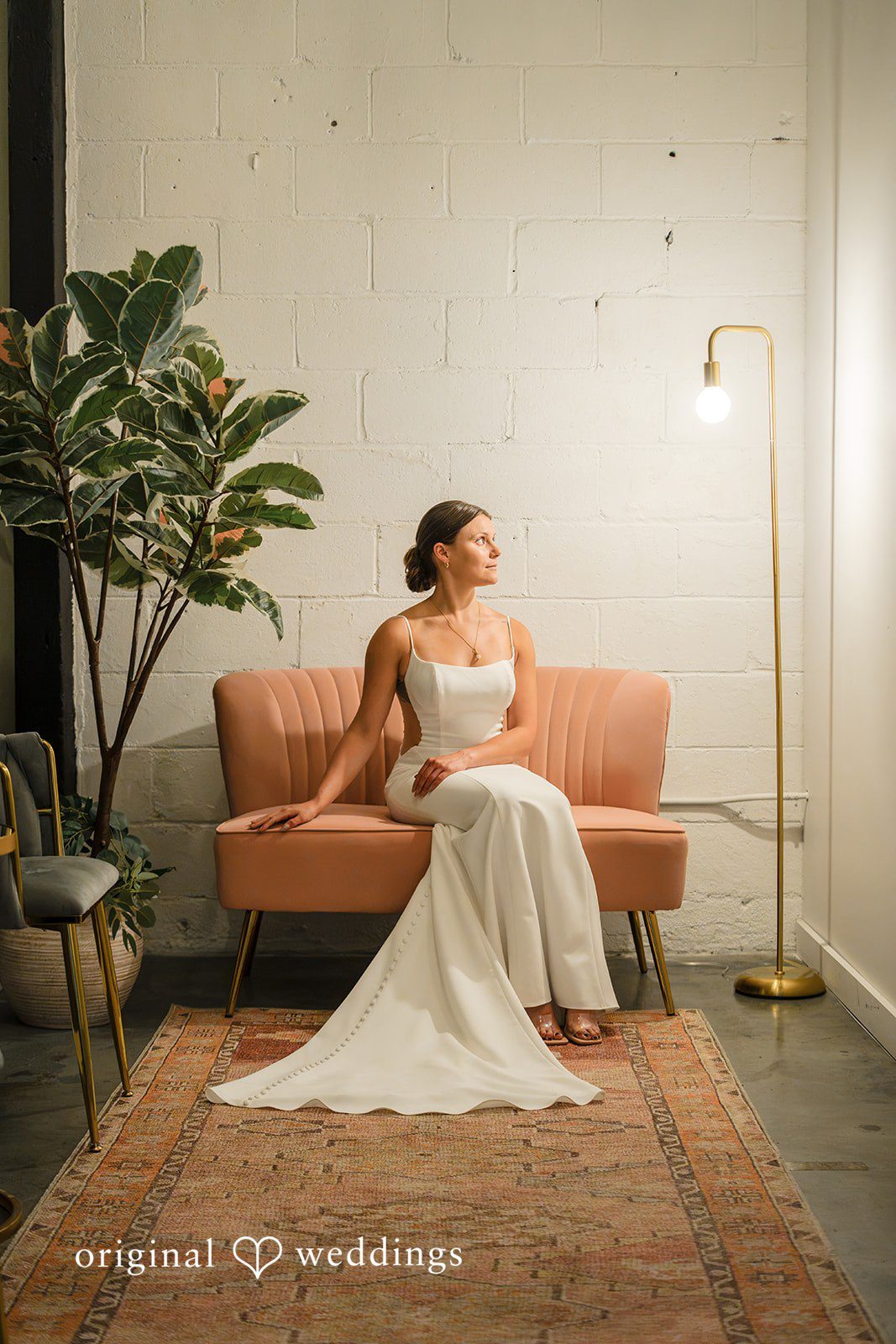 A bride sitting gracefully on an orange vintage sofa against a plain wall.