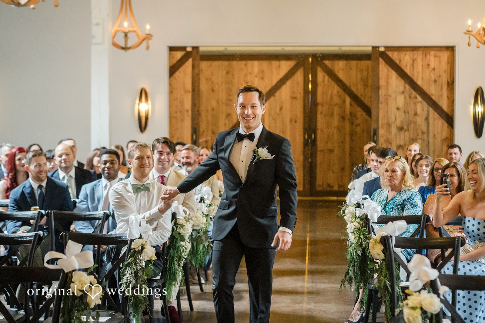 A groom walking down the aisle during a wedding ceremony surrounded by guests.