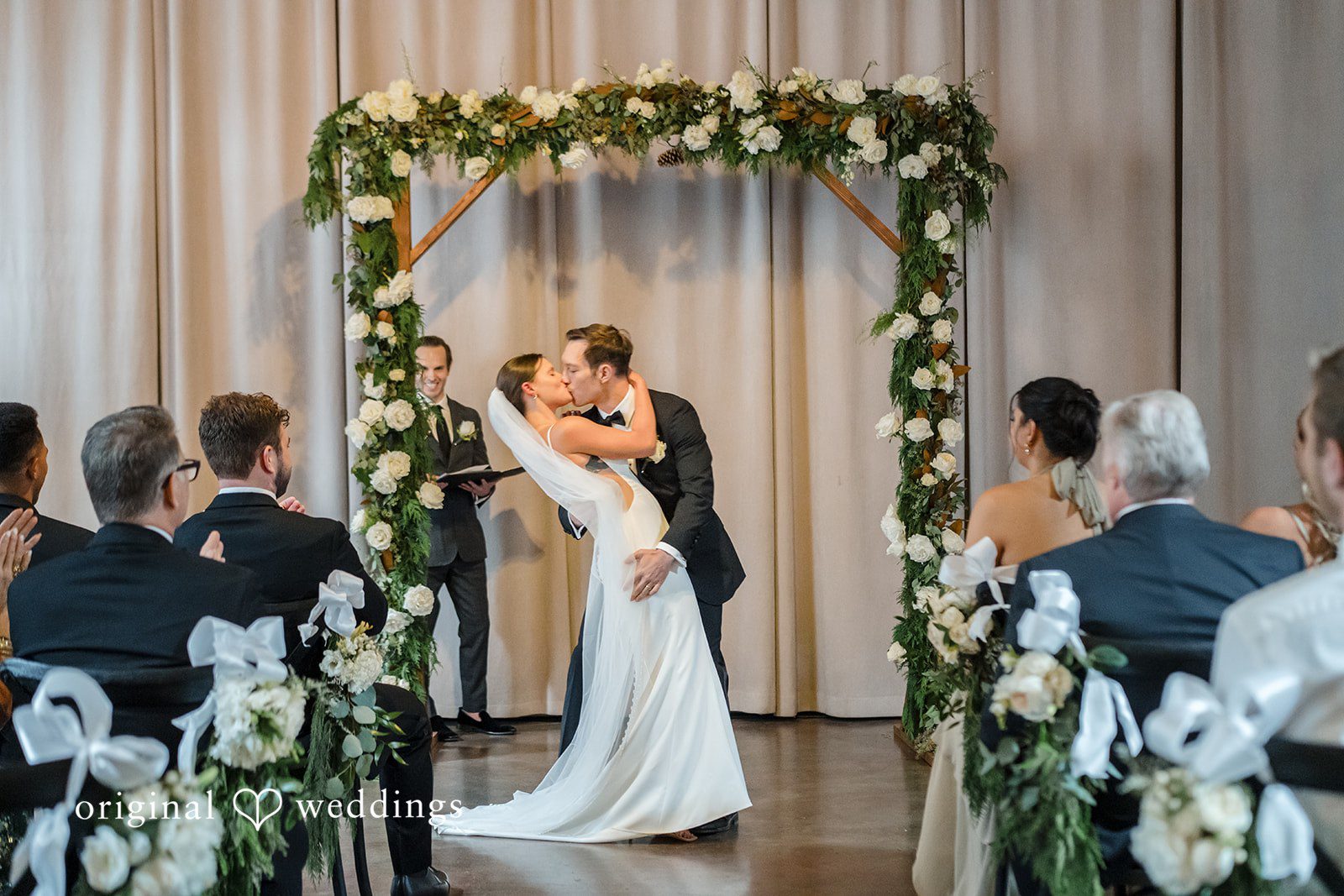 A bride and groom sharing a kiss at the floral altar during their wedding ceremony.