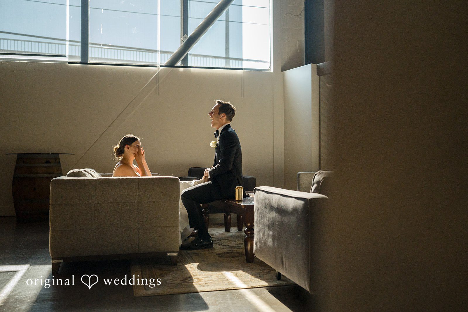 A bride and groom sitting together at a small table and sofa.