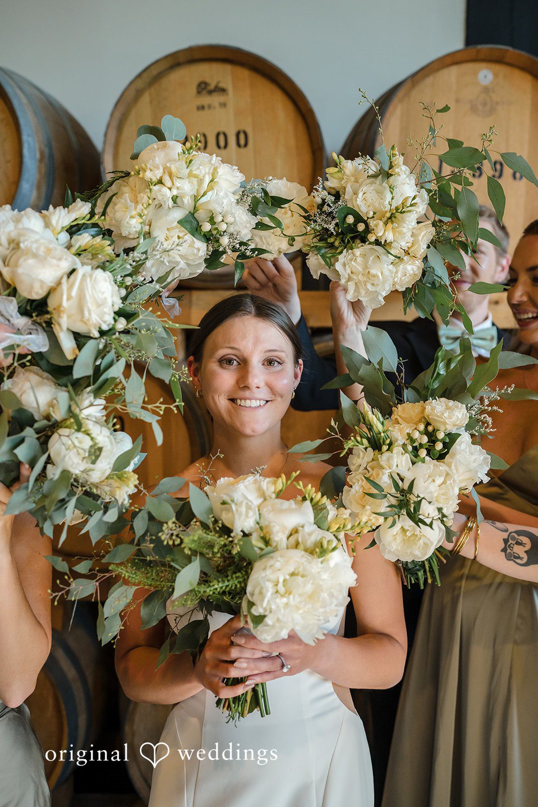 A bride smiling while holding a large, circular floral hoop bouquet.