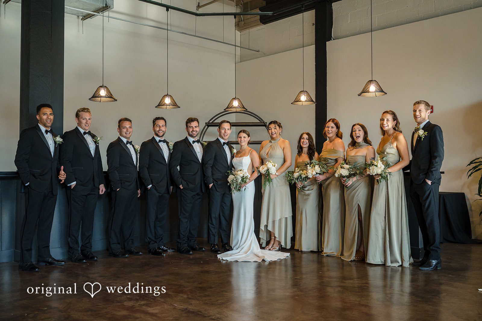 A large wedding party standing in a long line inside an industrial-style venue.