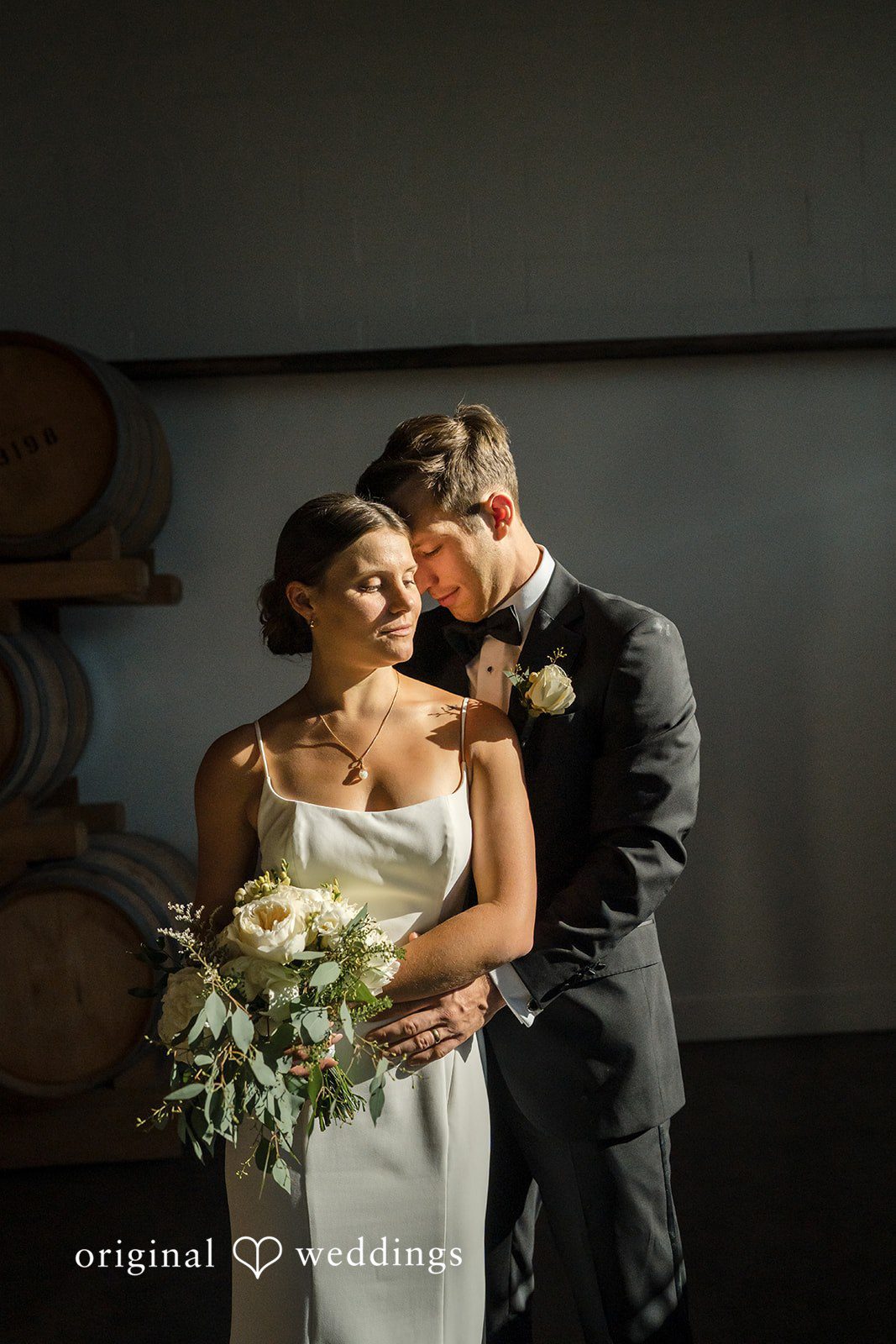 A bride and groom posing closely together while holding a bouquet.