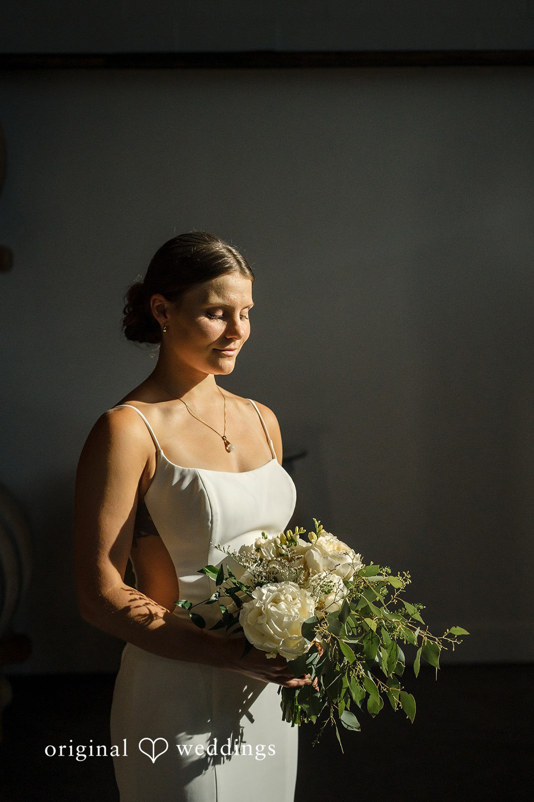 A bride in profile holding her bouquet under dramatic, moody lighting.