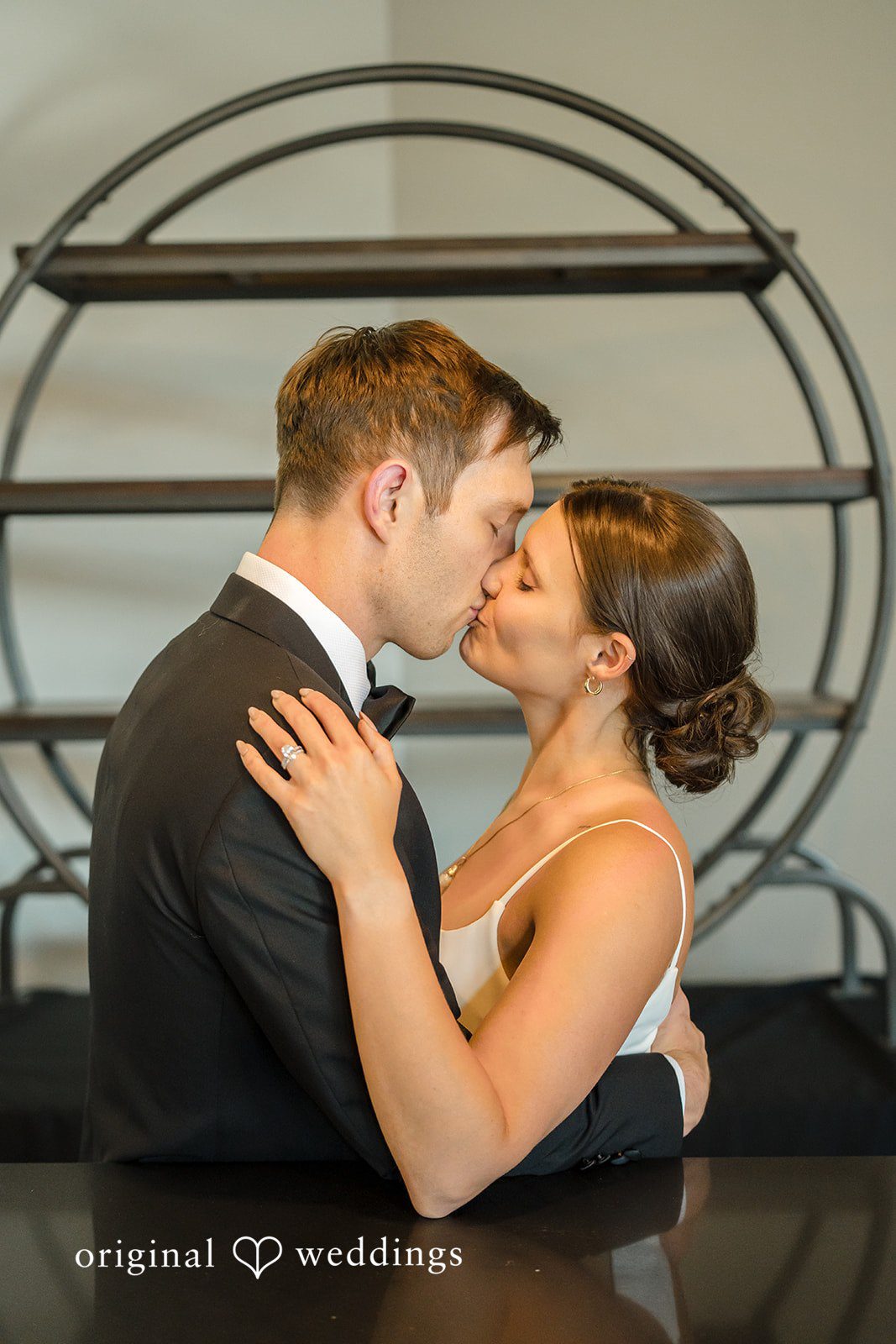 A bride and groom embracing and leaning in for a kiss.