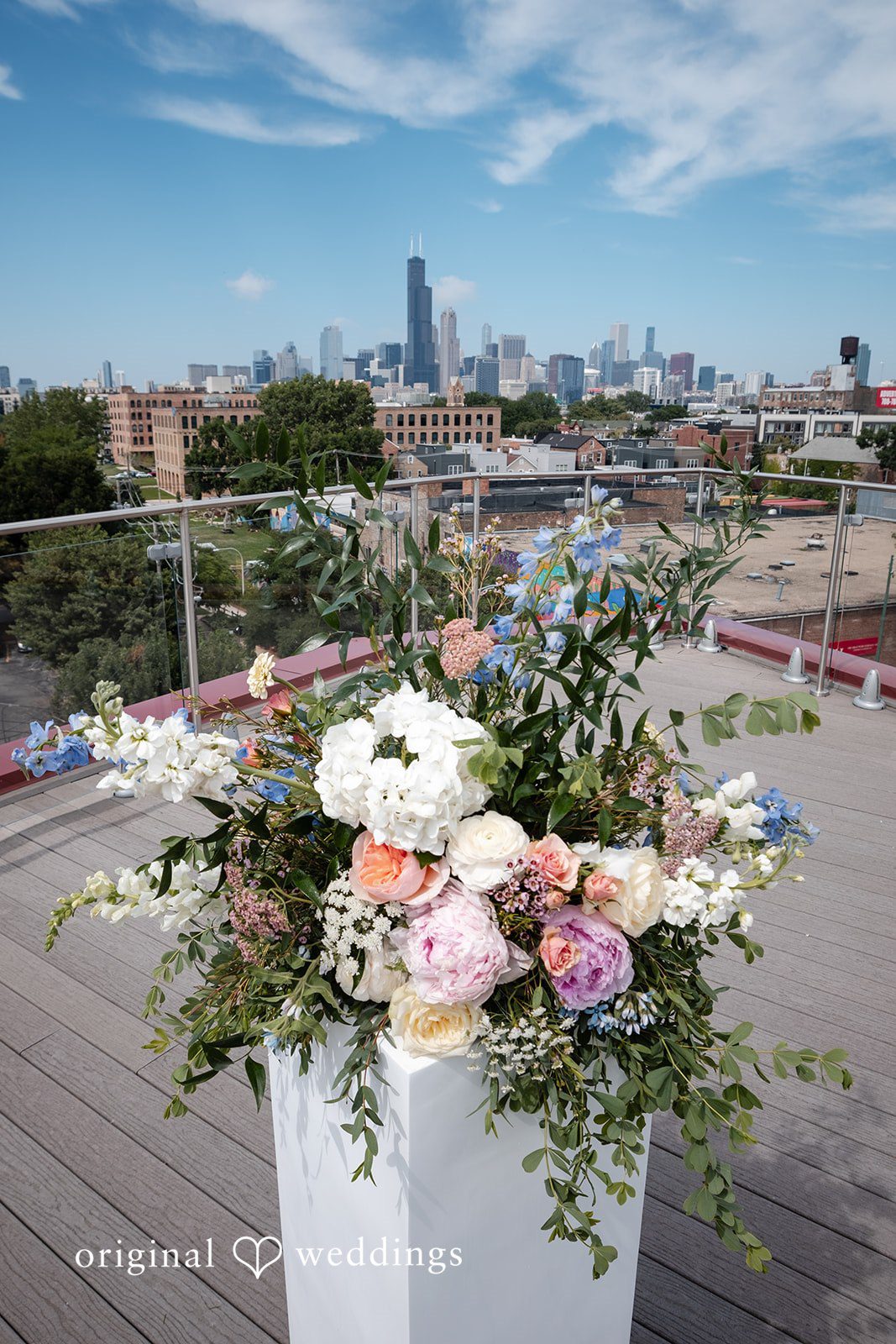 Lucy + Cormac A large floral arrangement placed on a rooftop railing with a city background.