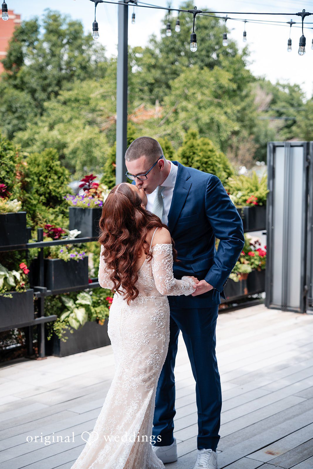 Lucy + Cormac A bride and groom embracing on a paved area with trees.