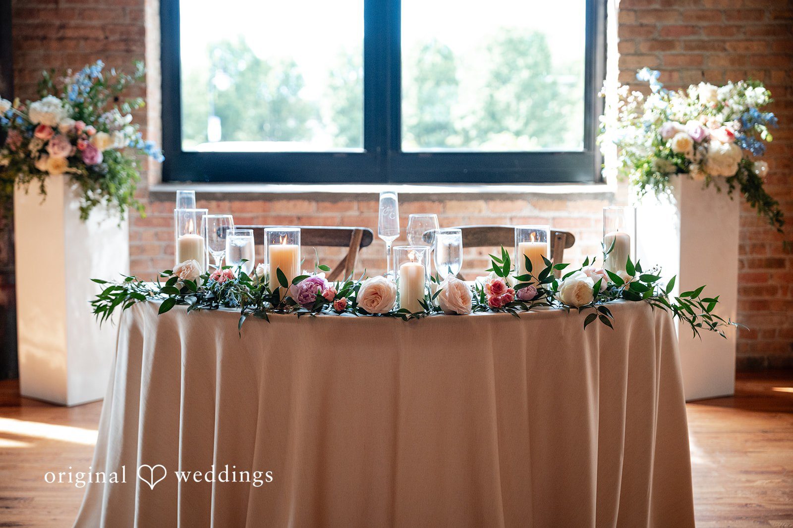 Lucy + Cormac A long wedding head table decorated with a light fabric tablecloth.