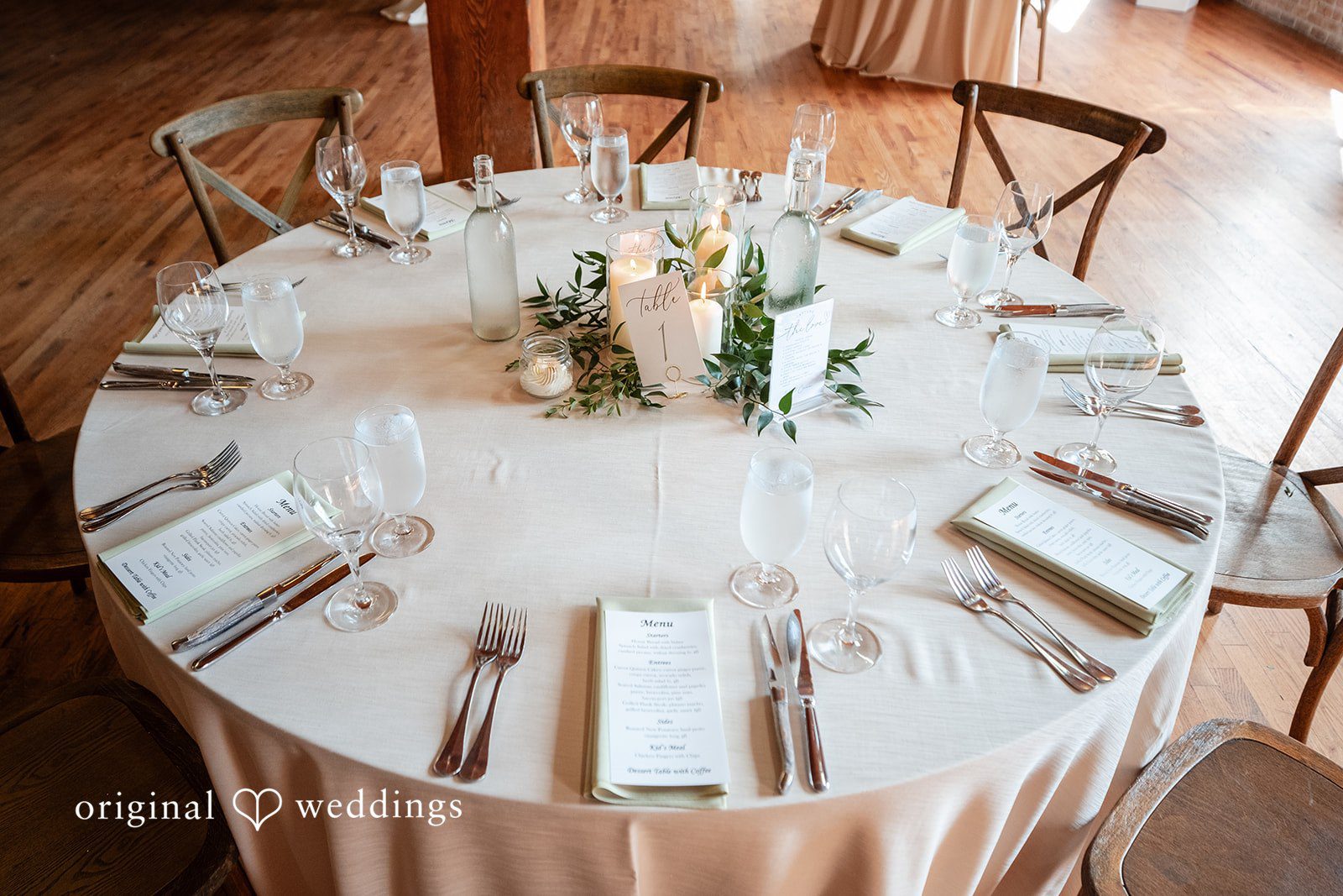 Lucy + Cormac A round reception table set with white dinnerware and a floral centerpiece.