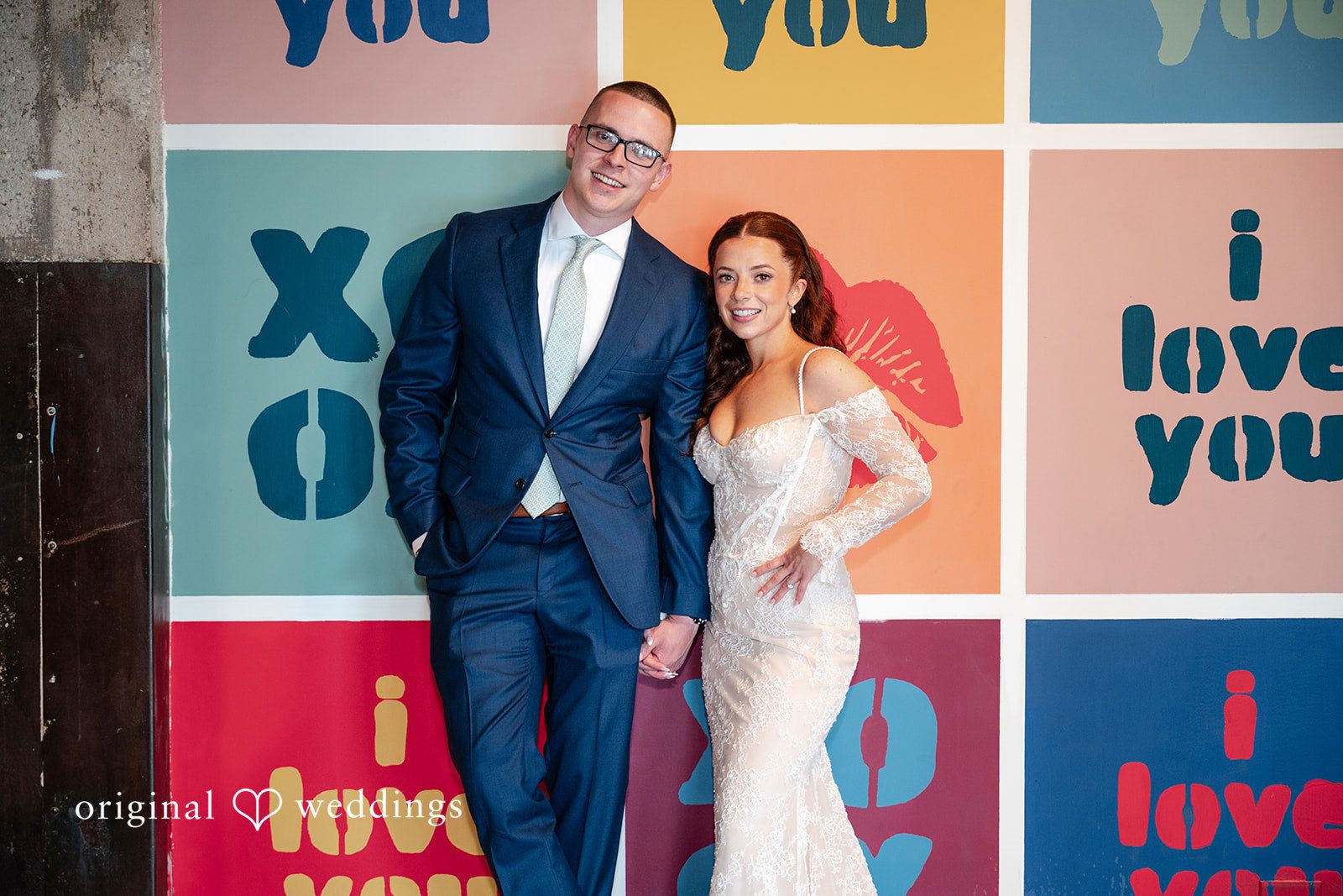 Lucy + Cormac A bride and groom standing together in front of a colorful graphic backdrop.
