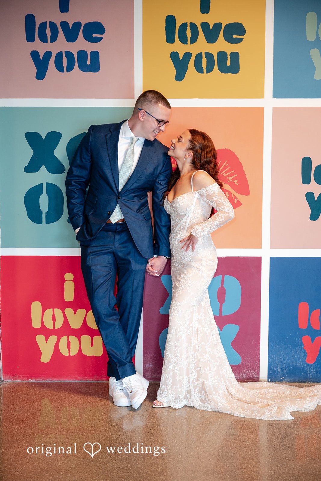 Lucy + Cormac A bride and groom posing in front of a backdrop featuring text and symbols.