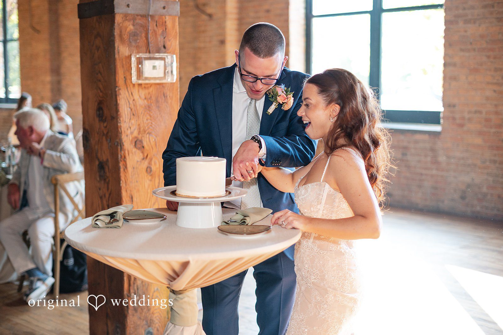 Lucy + Cormac A bride and groom standing next to a round table cutting their wedding cake.
