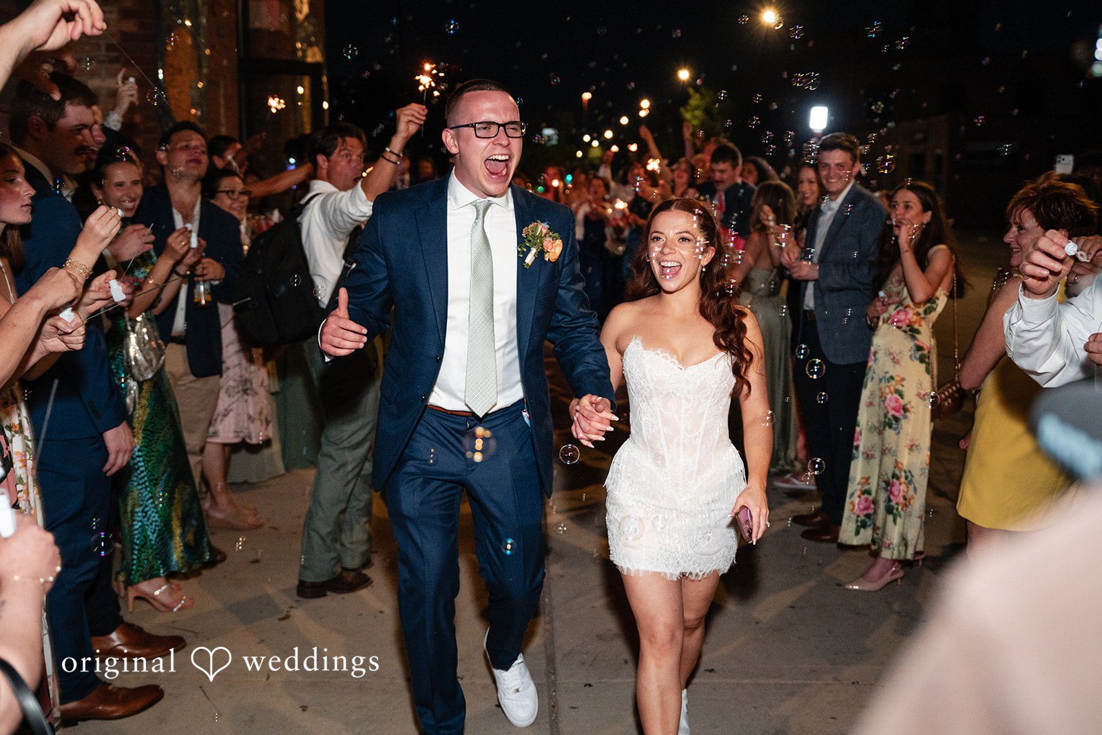 Lucy + Cormac A bride and groom walking through a crowd of cheering wedding guests.