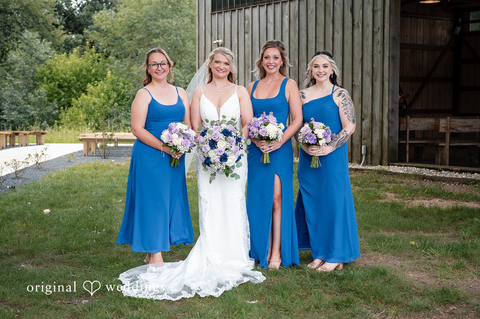 Bride and bridesmaids posing together wearing matching long royal blue dresses.