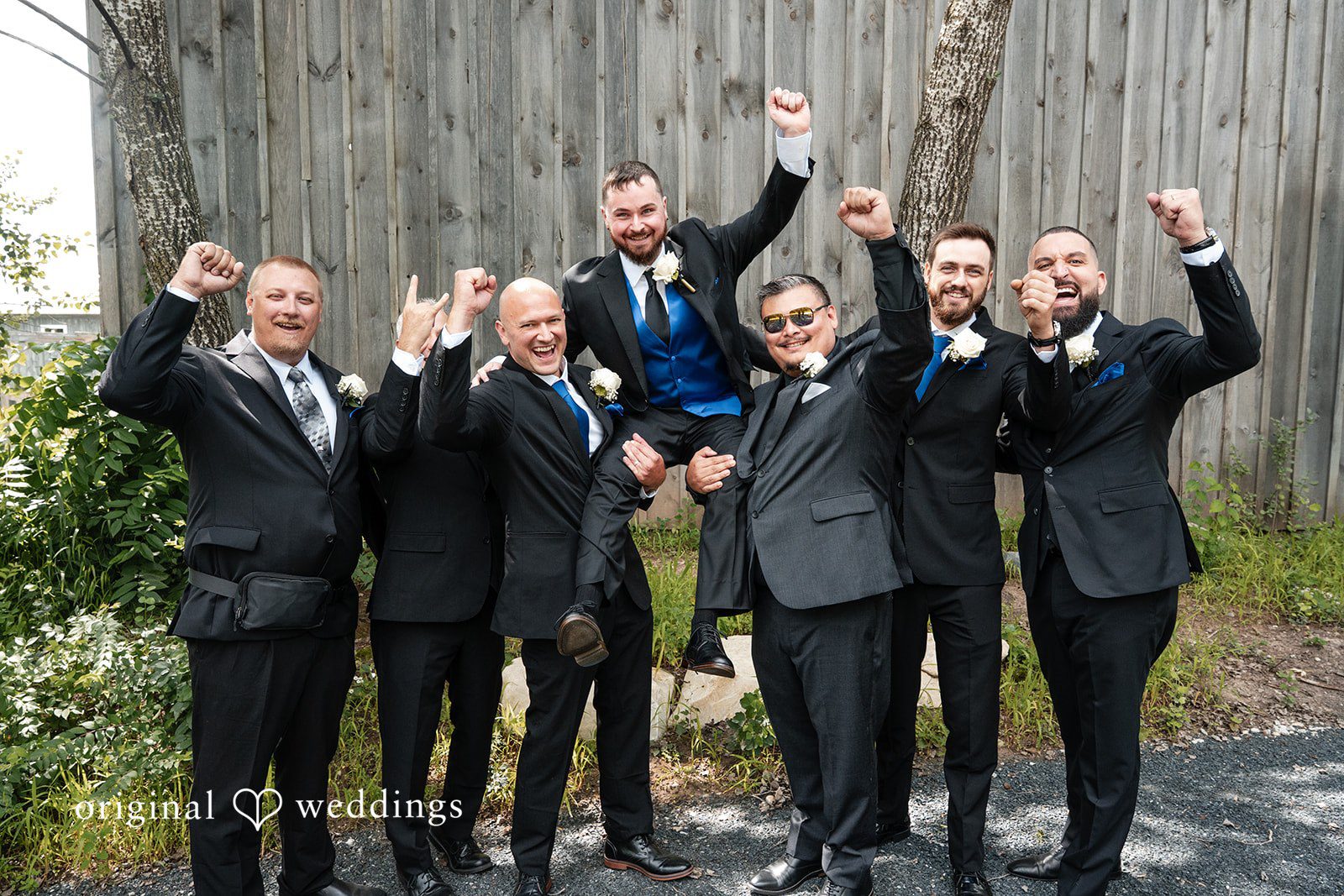 Groom and groomsmen cheering with their arms raised in the air.