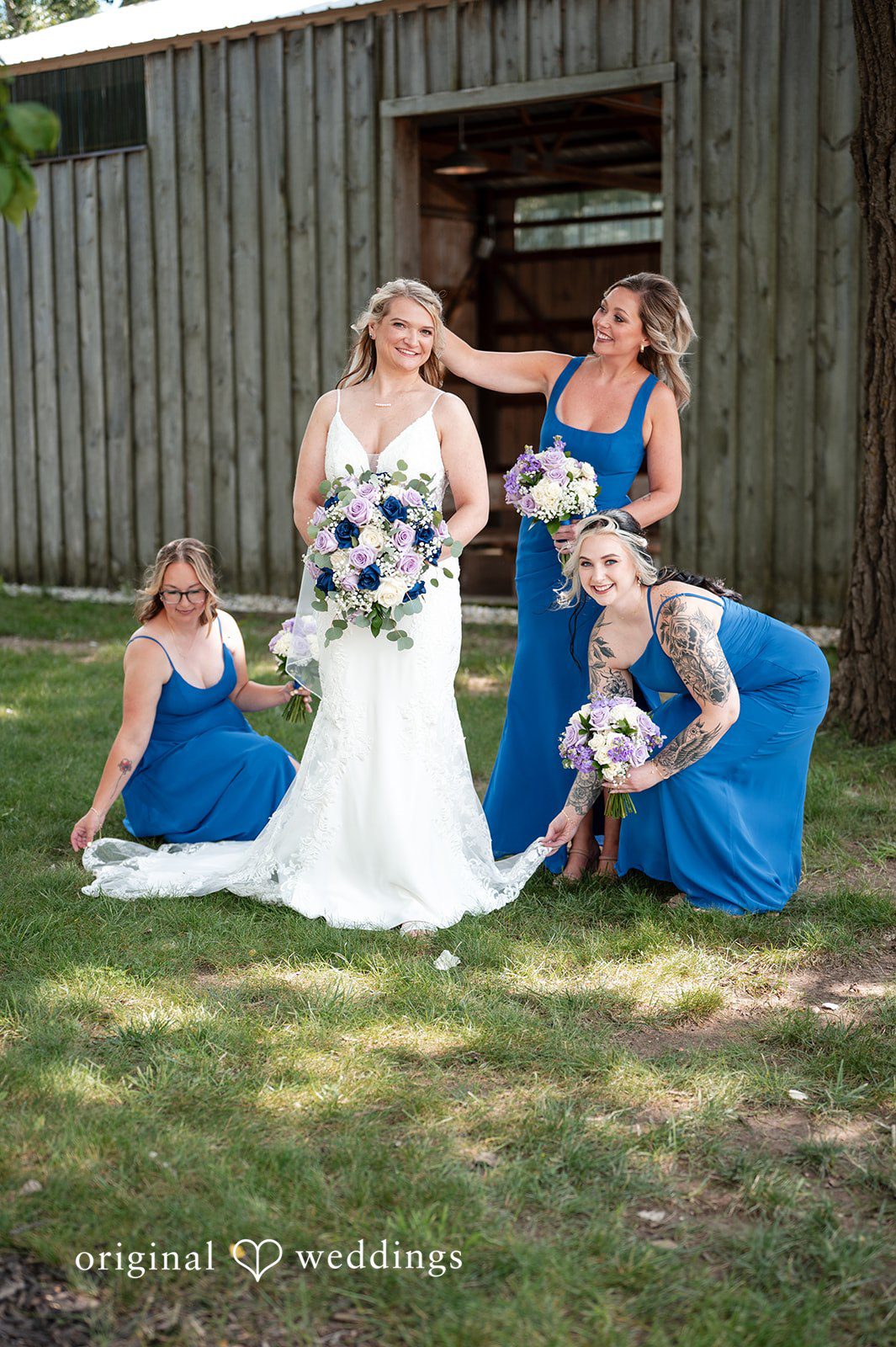 A bride sitting on grass surrounded by her bridesmaids in blue dresses.