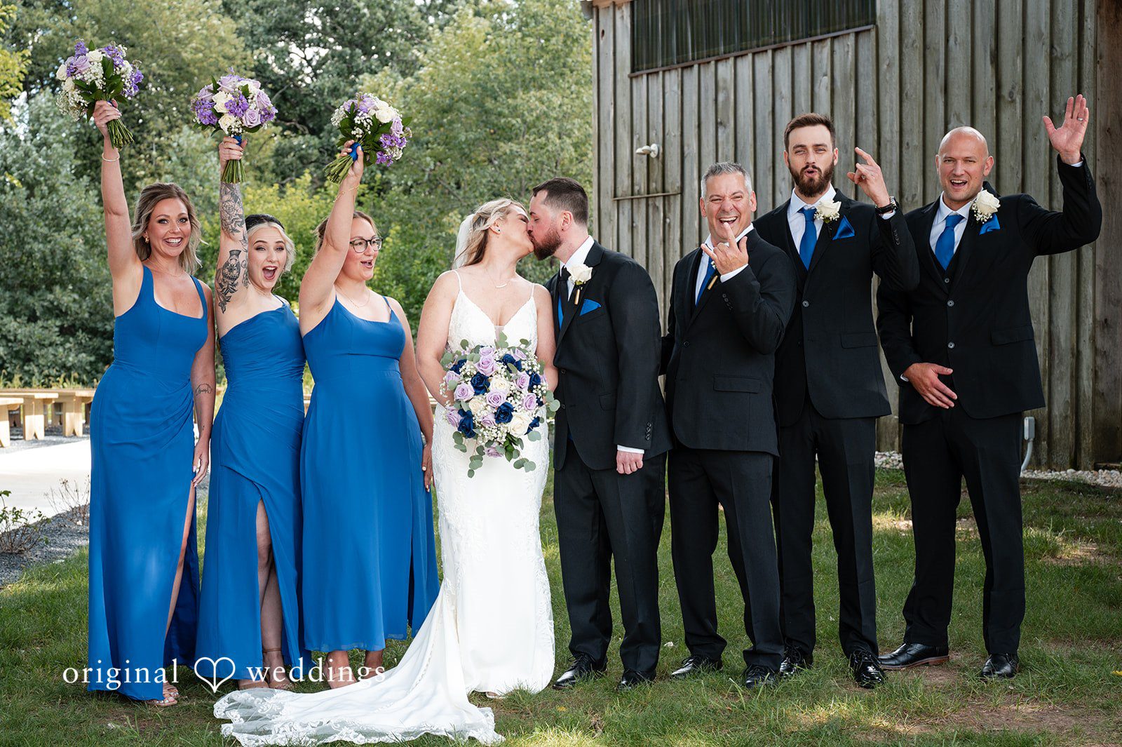 A bridal party in blue dresses posing alongside a group of groomsmen in suits.