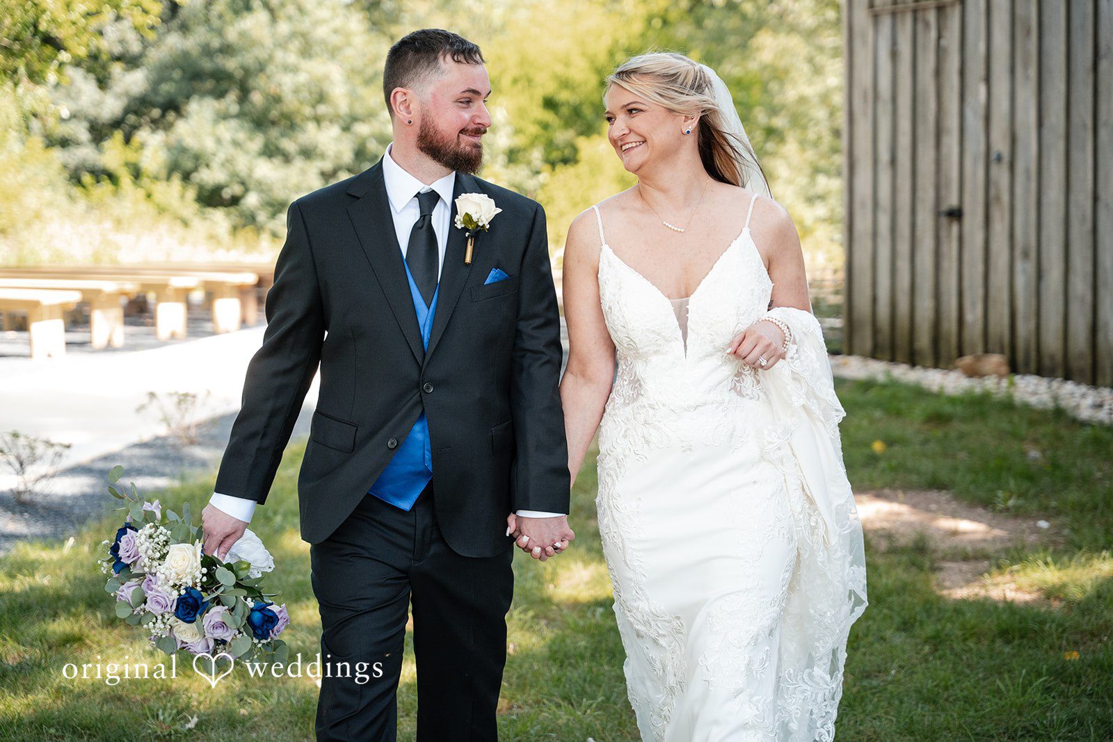 A bride and groom walking hand-in-hand while smiling at each other.