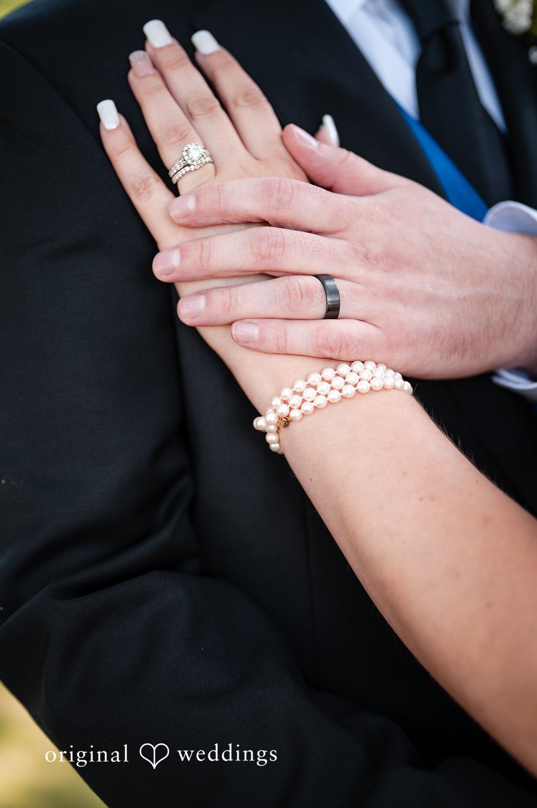 Close-up of a bride holding the groom's hand, showcasing her wedding ring and bracelet.