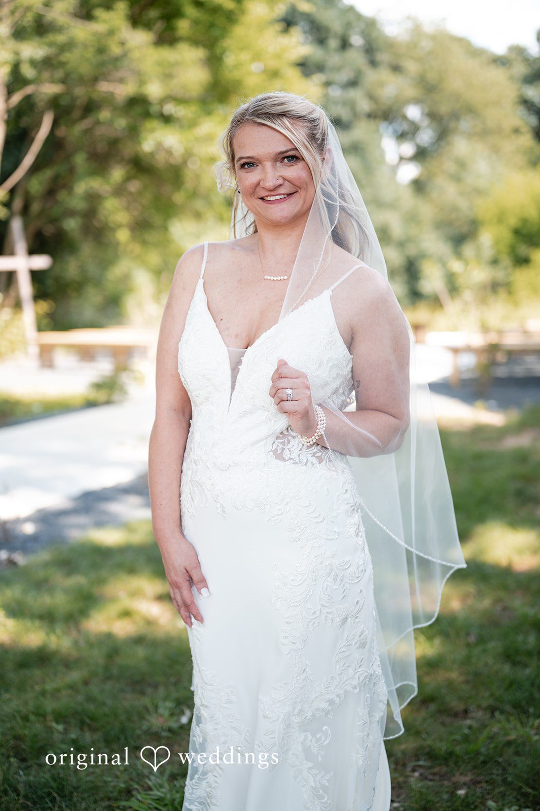 A smiling bride posing in a white lace dress with a veil.