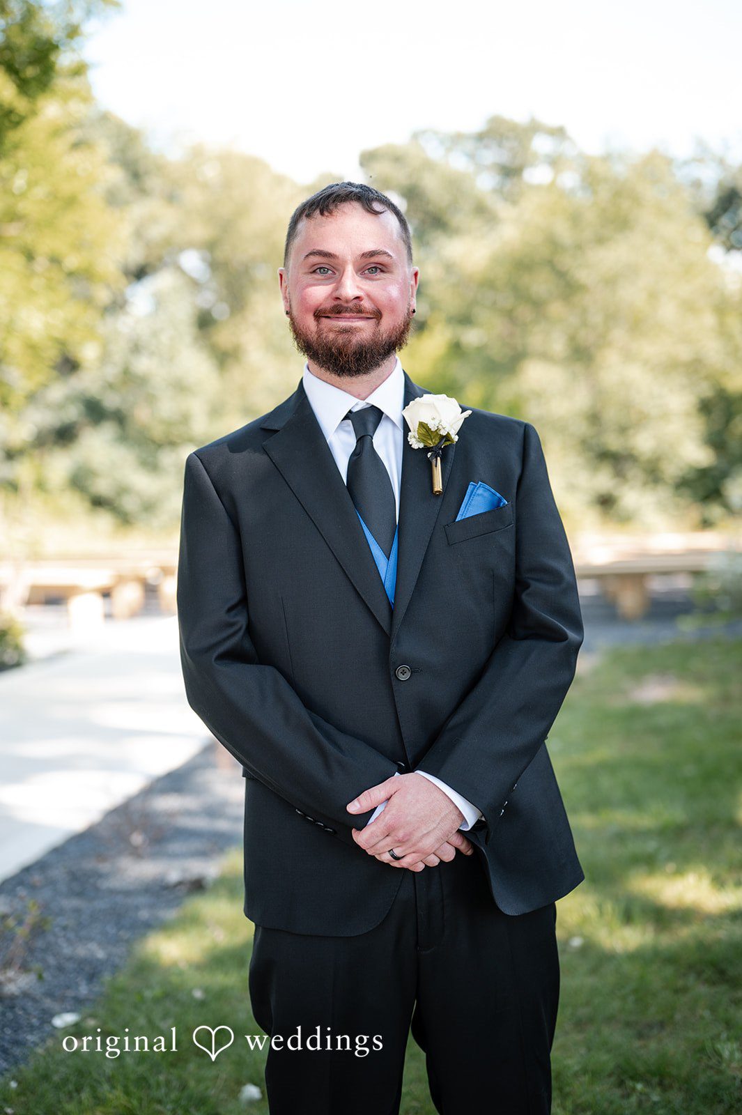 A groom smiling in a black suit with a blue tie.