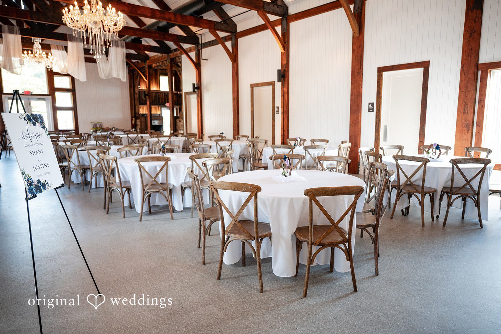 Round reception tables set up with white tablecloths and wooden chairs.