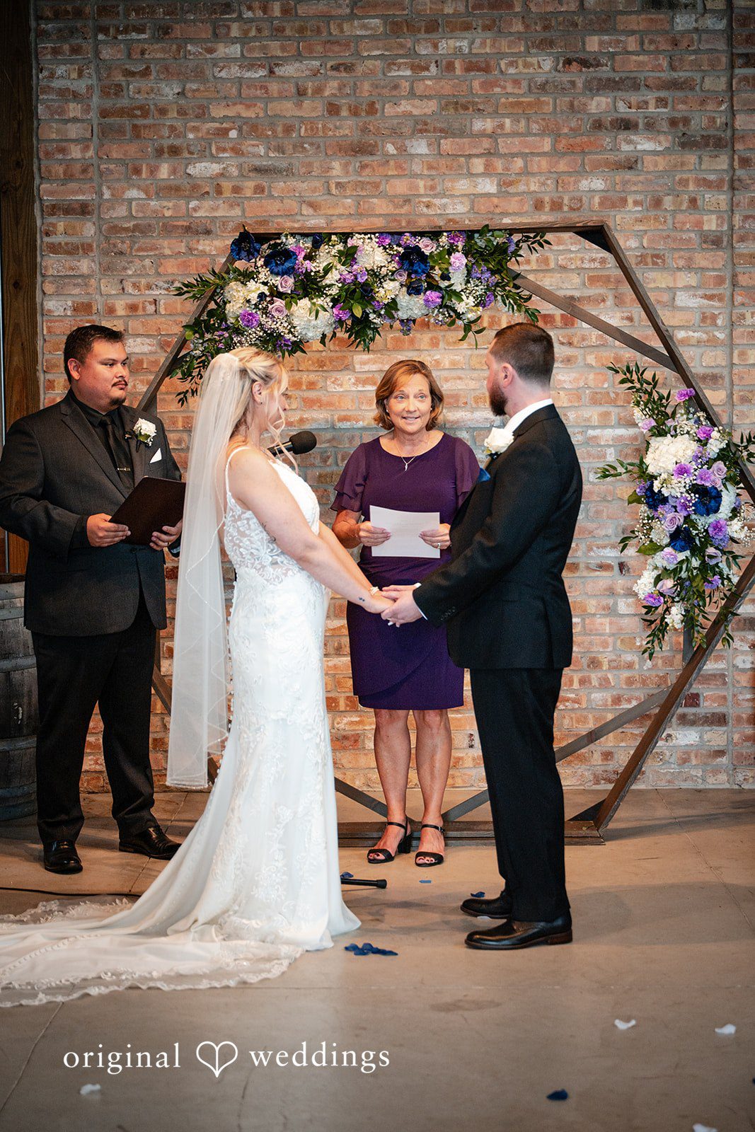 A bride and groom exchanging vows under a circular floral arch.