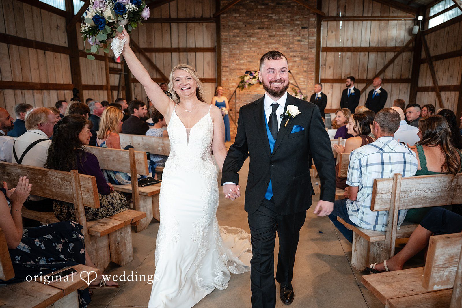 A newly married bride and groom walking up the aisle cheering.