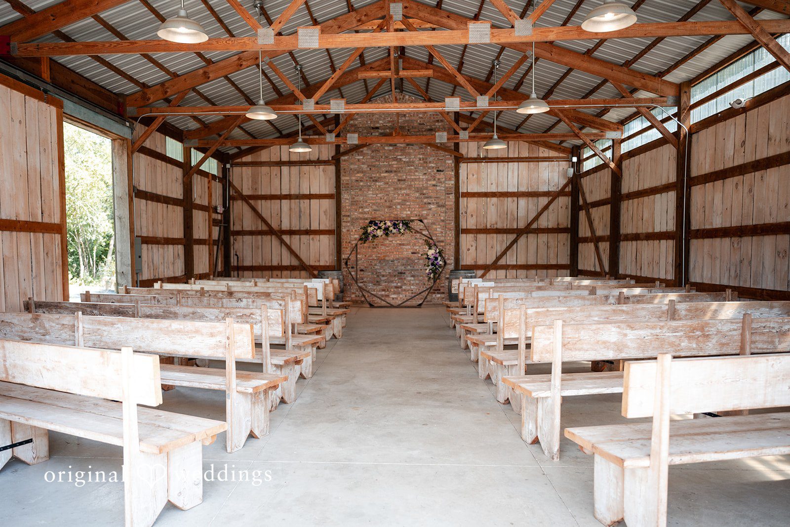 Rows of empty wooden benches set up for a ceremony inside a rustic barn.