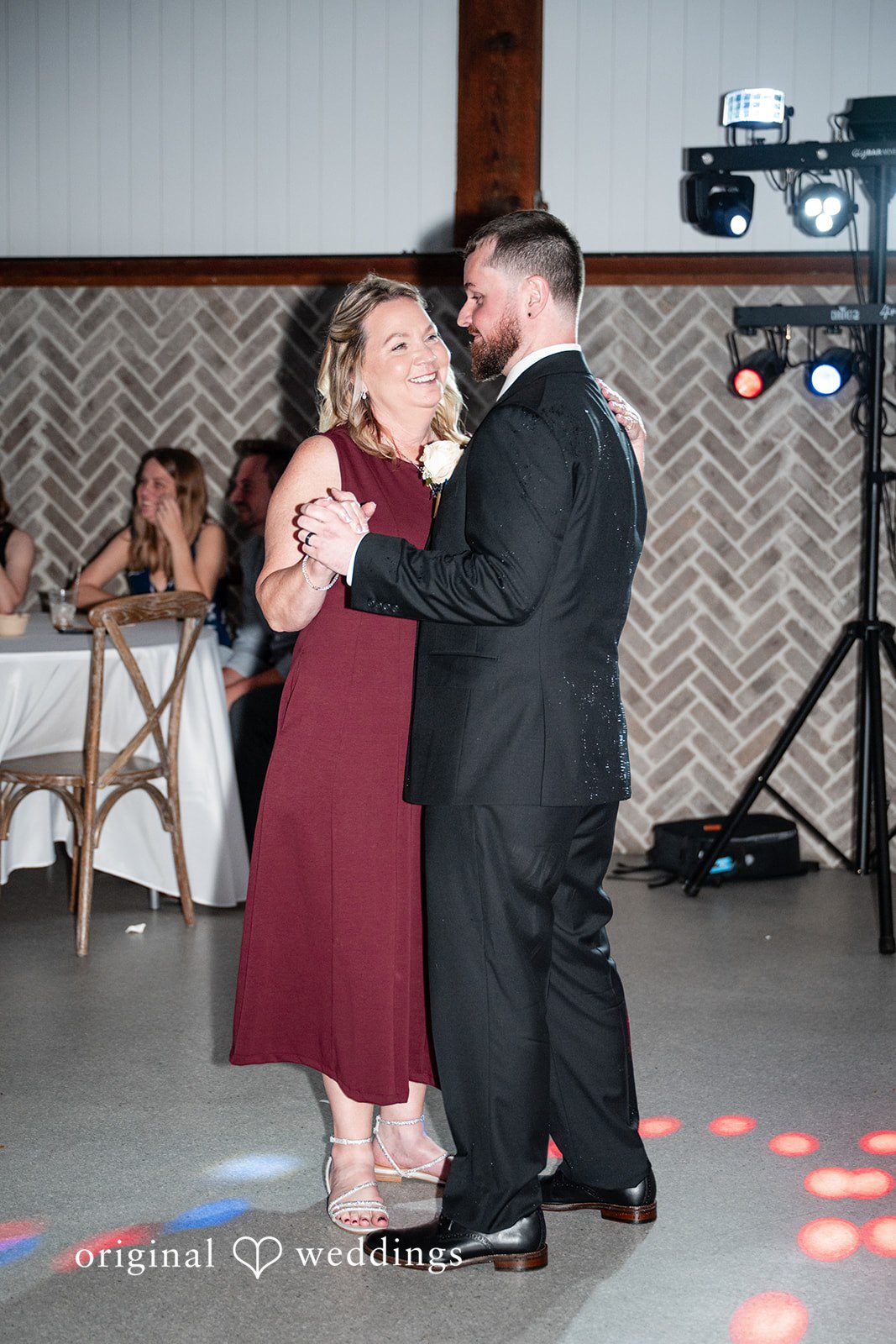 A groom and a woman in a maroon dress dancing together at a wedding reception.