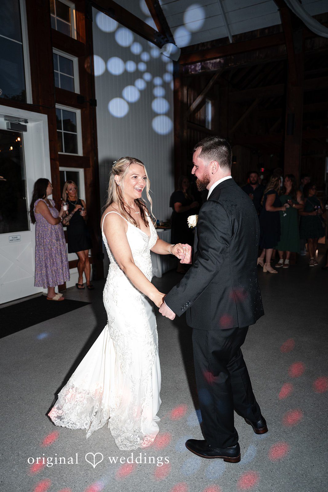 A bride and groom dancing together under colorful reception lights.