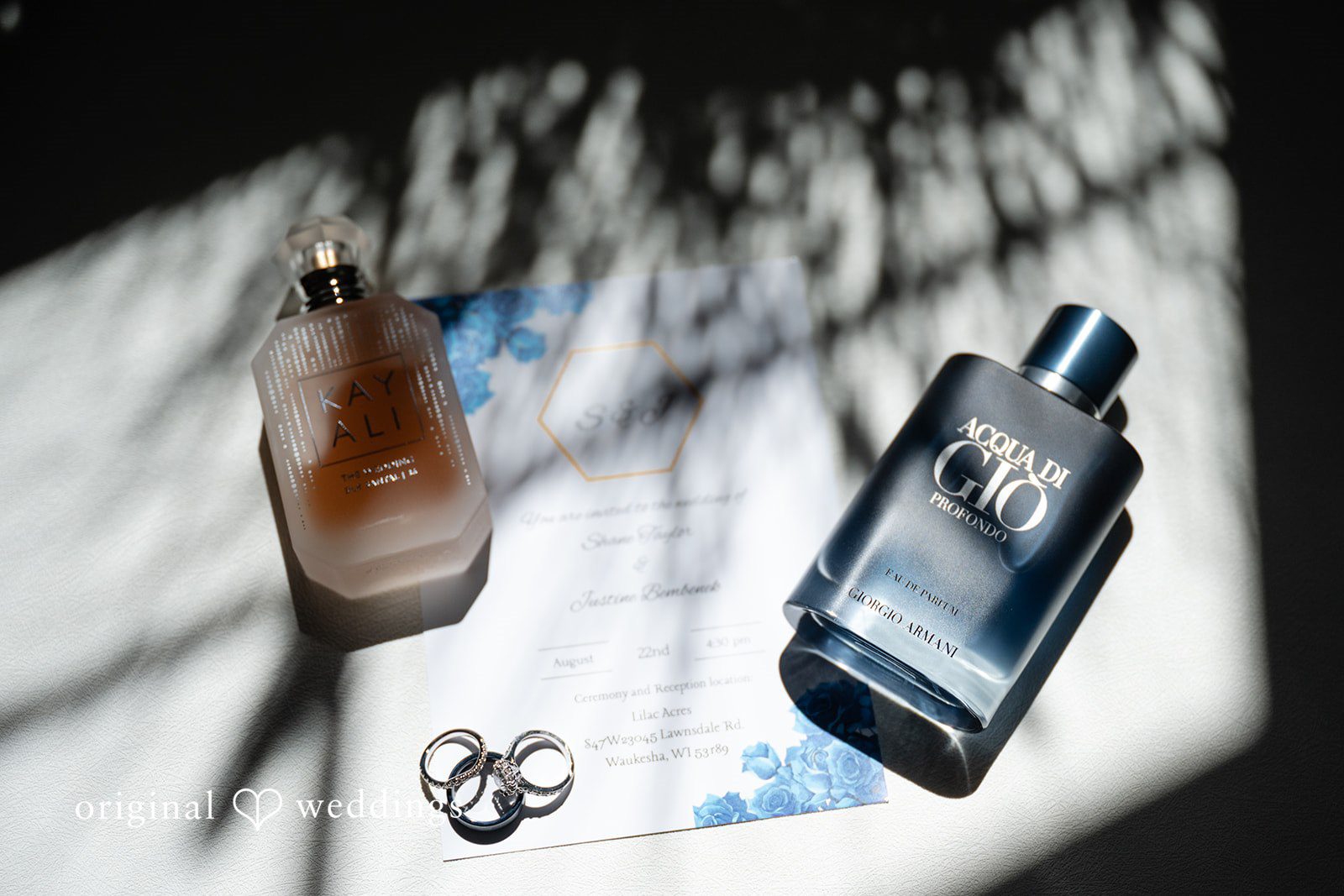 Flat-lay of wedding details including cologne, a watch, and rings.