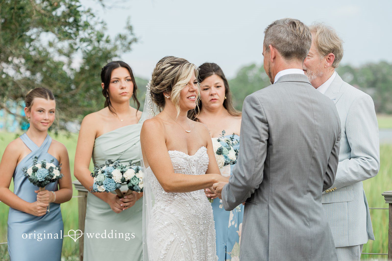 Jennifer + Zac Bridesmaids in light blue dresses standing in a line at a wedding ceremony.