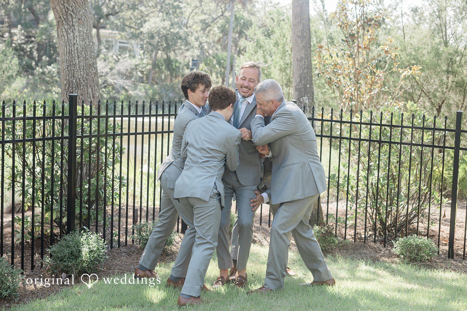 Jennifer + Zac A groom posing with his groomsmen in grey suits against a black metal fence.