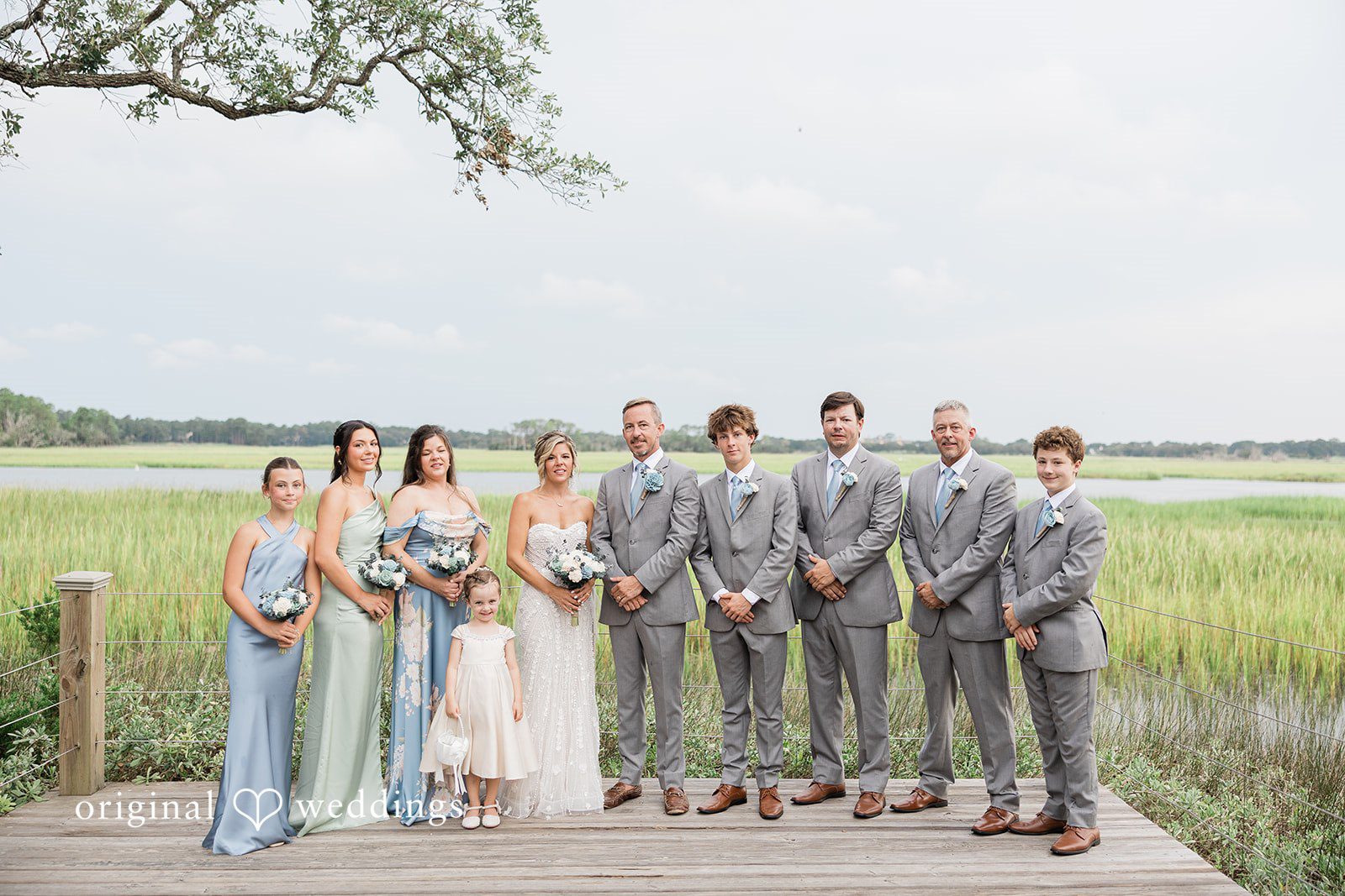 Jennifer + Zac A large wedding party posing together for a group photo on a wooden dock.