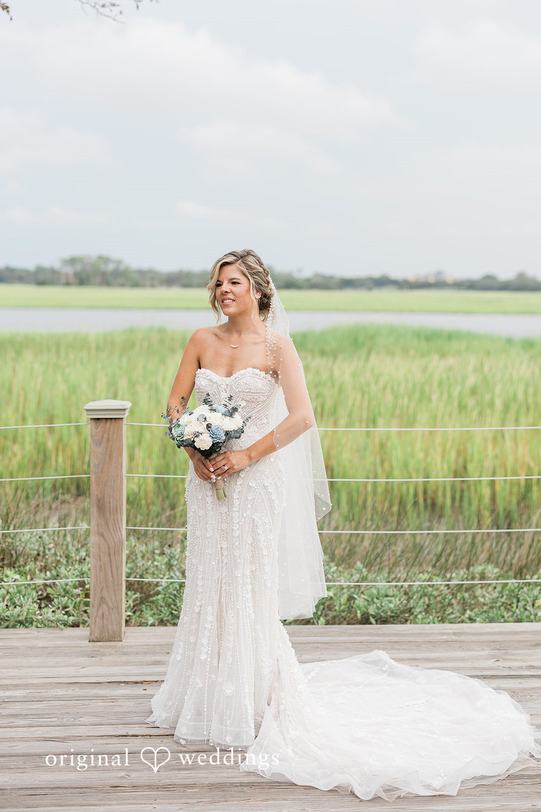 Jennifer + Zac A bride in a strapless gown walking across a grassy field near a wooden fence.