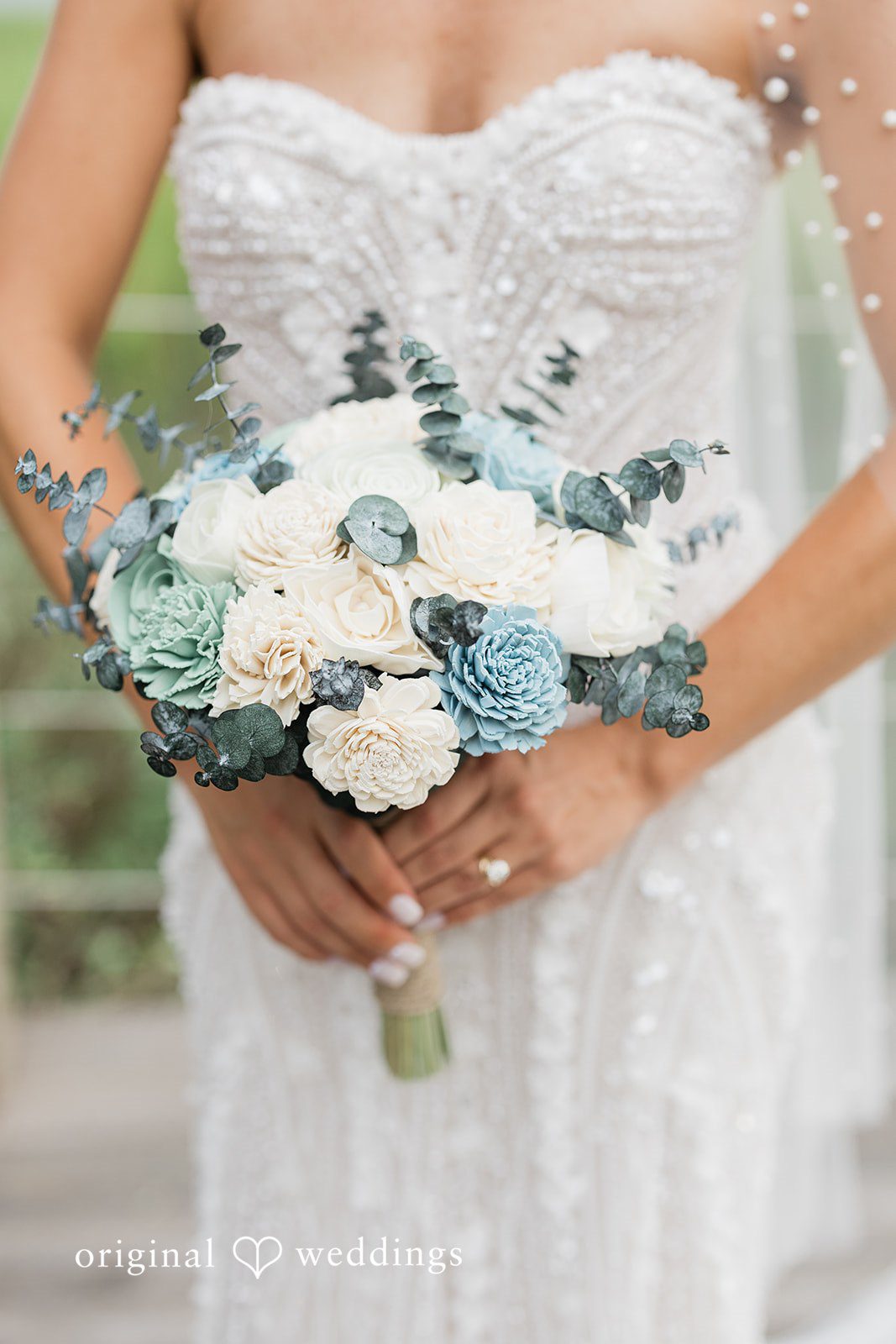 Jennifer + Zac A close-up of a bride holding a bouquet of white flowers with blue accents.