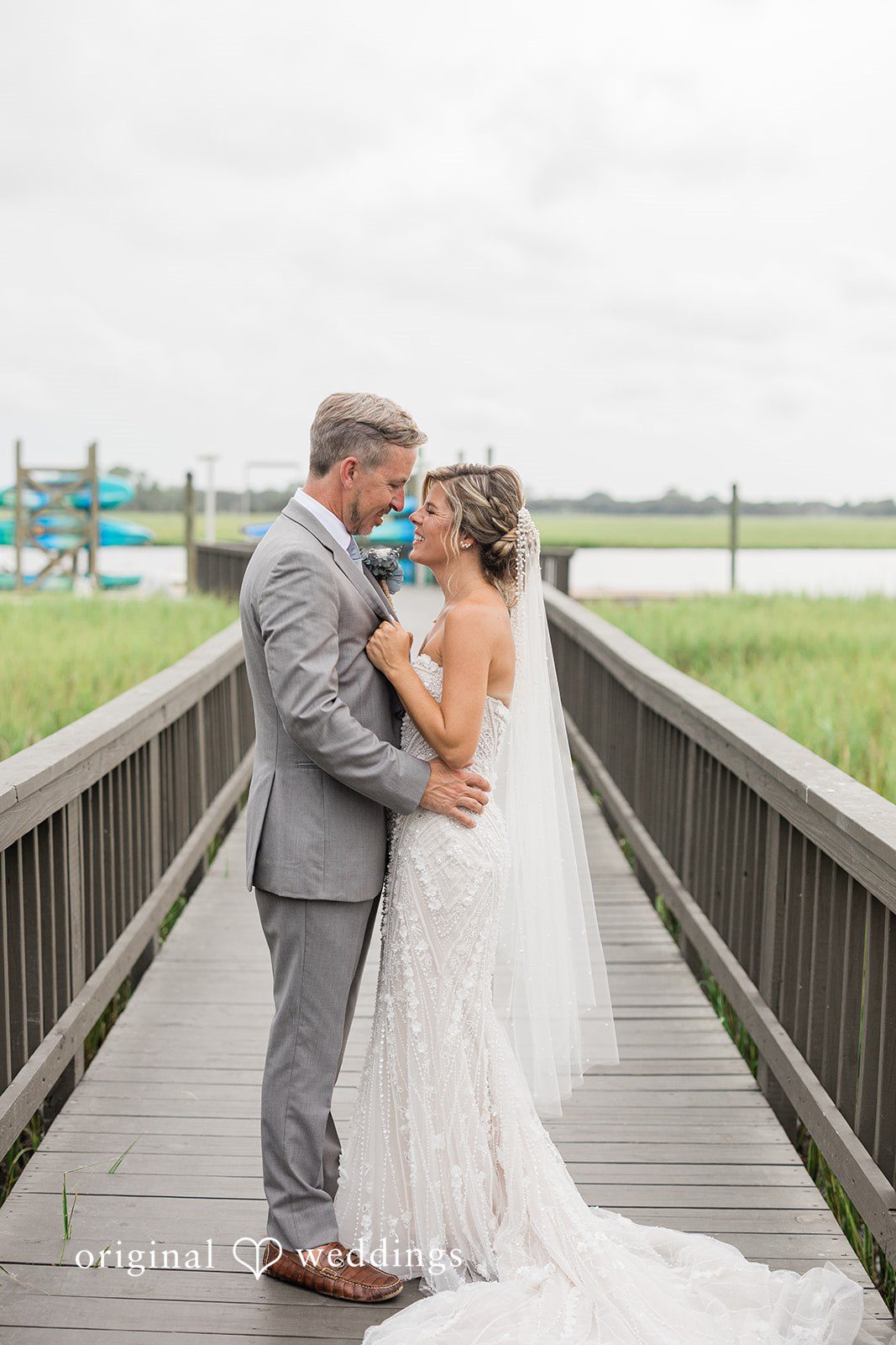 Jennifer + Zac A bride and groom posing together on a wooden walkway with a scenic background.