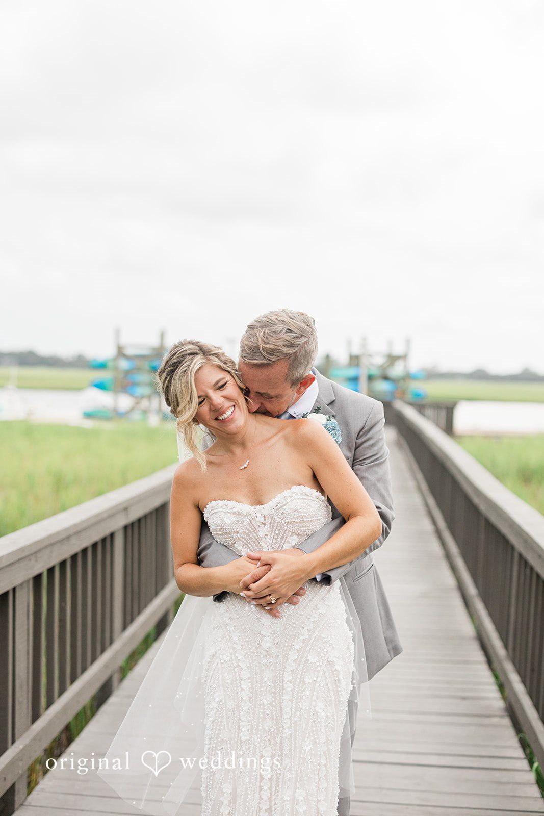 Jennifer + Zac A bride and groom embracing while posing on a wooden dock over the water.