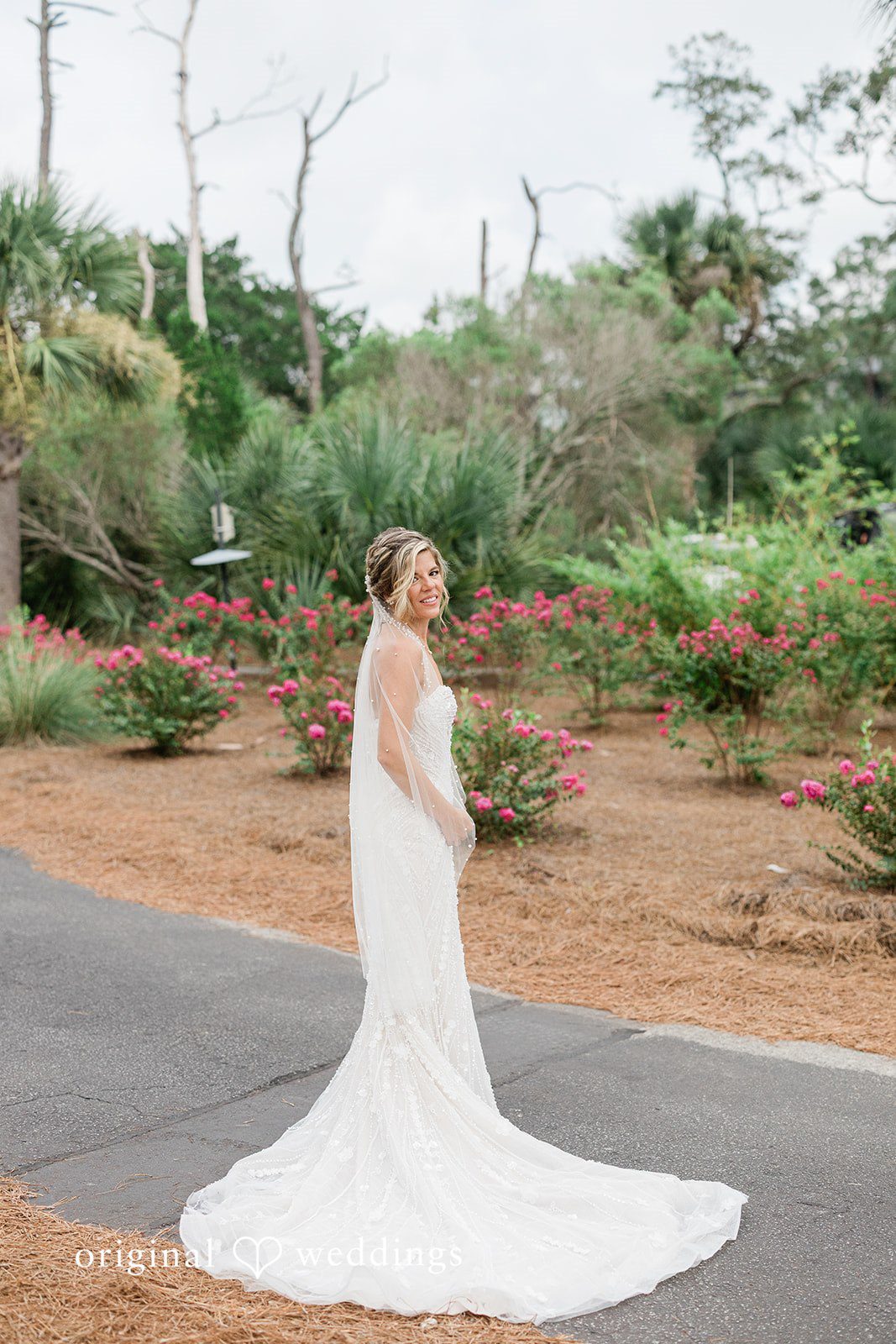 Jennifer + Zac A bride in a white wedding gown standing on a paved pathway surrounded by greenery.