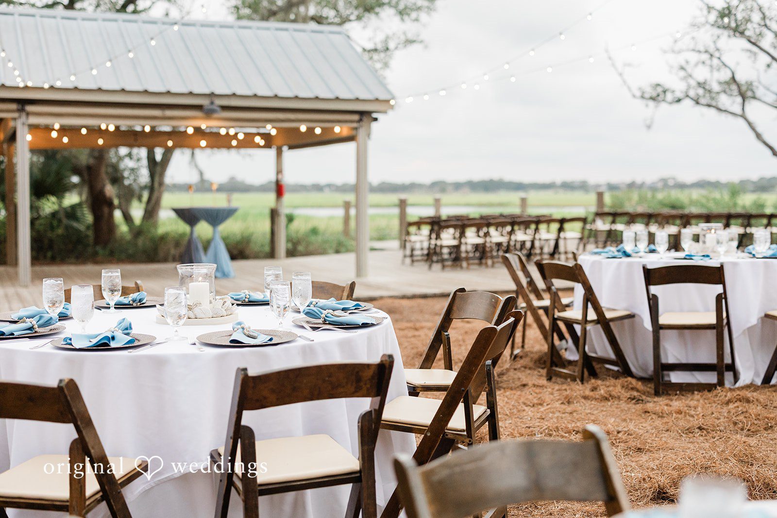Jennifer + Zac A decorated wedding reception table with white linens and wooden chairs in an open barn venue.