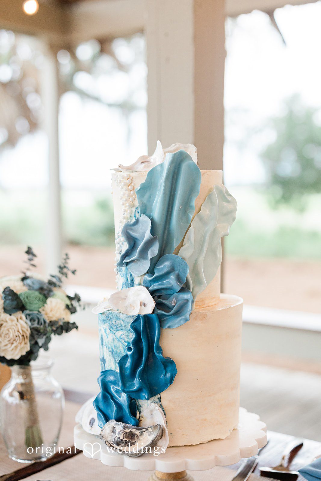 Jennifer + Zac Wedding cake decorated with cascading blue fabric ribbons on a reception table.
