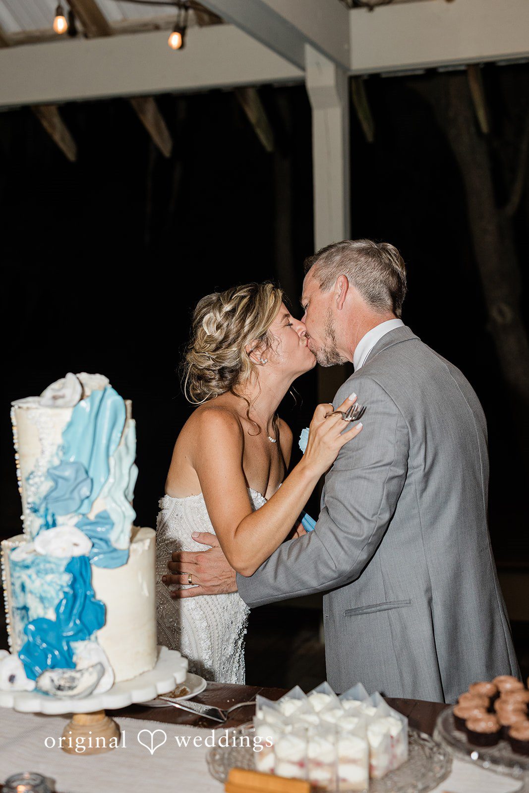 Jennifer + Zac A bride and groom sharing a kiss next to their blue and white wedding cake.