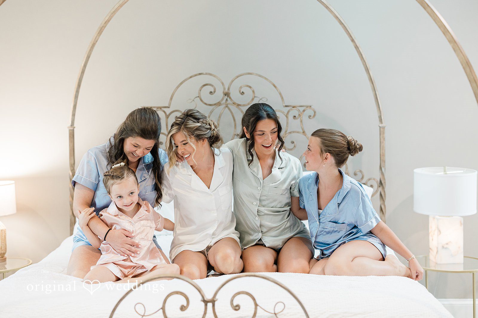 Jennifer + Zac A group of bridesmaids in matching blue pajamas sitting together on a bed.