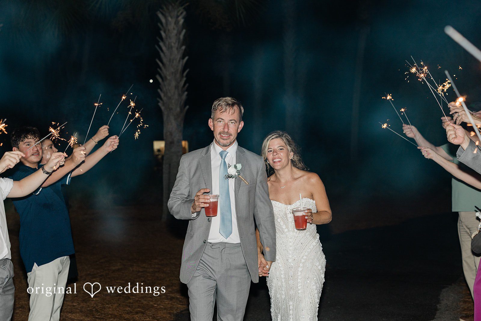 Jennifer + Zac A bride and groom walking through a pathway of guests holding lit sparklers at night.