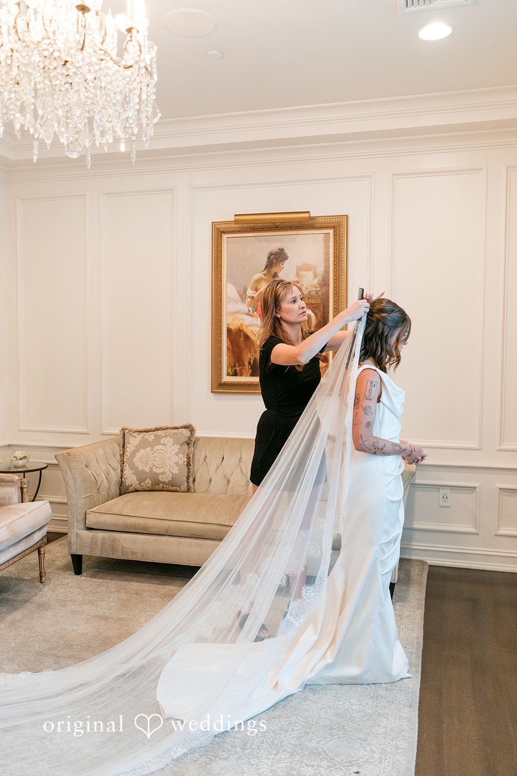 A bride with a long lace veil standing in a living room space.