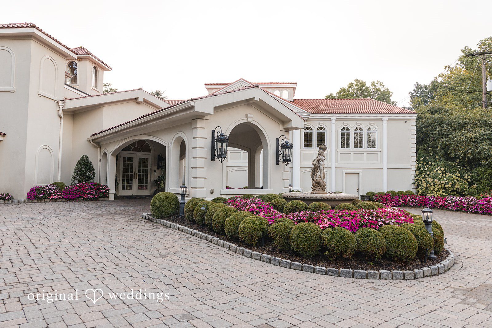A stone chapel building with flower beds and a curved walkway in front.