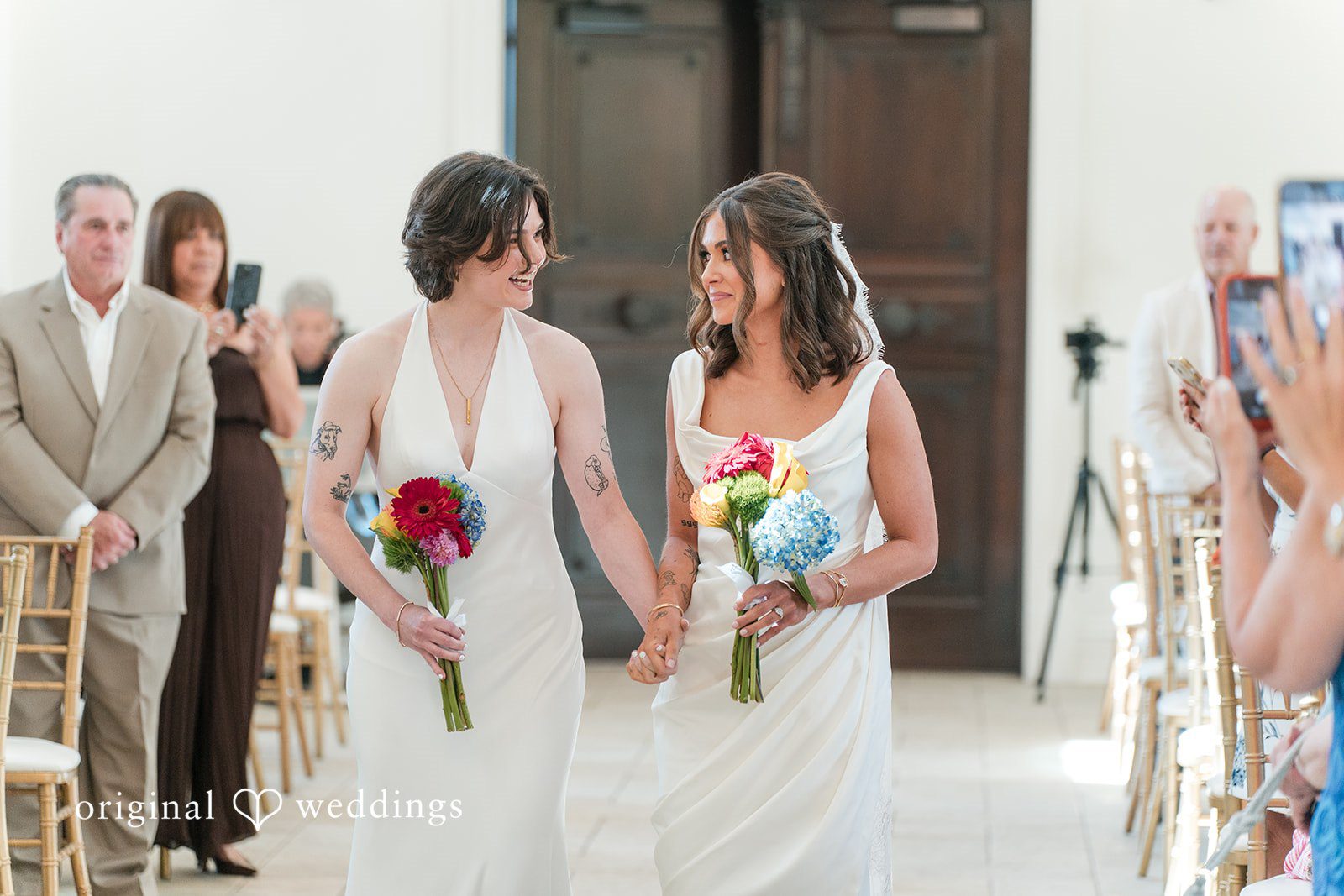 Couple holding bouquets while standing among guests at their wedding.